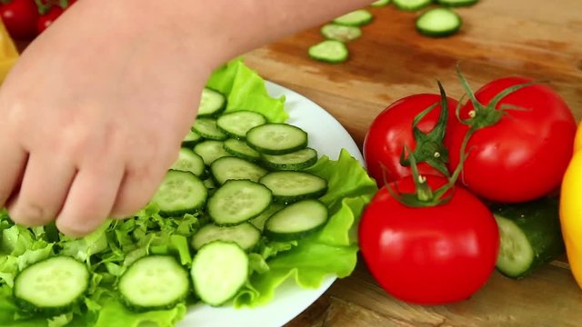 Preparation of homemade vegetable salad with cherry tomatoes, cheese and quail eggs. Female hands put in a bowl of sliced cucumbers. Close-up