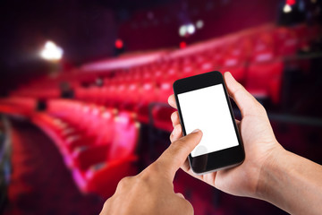 Smartphone on hand and white screen with blurry background of seat in movie theater.