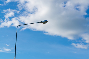 Street light lamp against the blue sky and tree background.