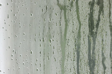 Detail of moisture dripping down glass with a green tint.