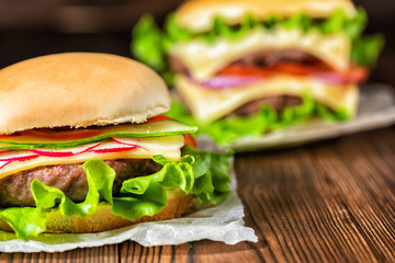 two homemade full cheeseburgers with vegetables, spices and beef meat on dark wooden background, close up
