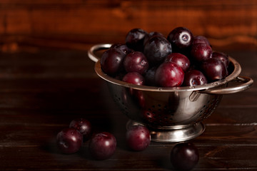 Ripe plums in a colander on a wooden background. Macro photo.