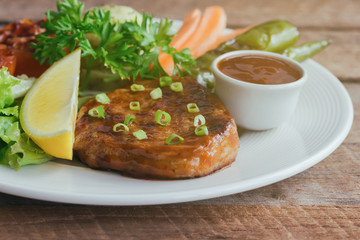 Barbecue pork steak on white plate served with barbecue sauce and vegetables. Pork steak for lunch or dinner on wood table. Moist and soft homemade pork barbecue served with mash potato and vegetable.
