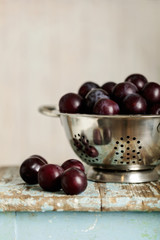 Ripe plums in a colander on a wooden background.