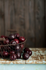 Ripe plums in a basket on a wooden background.