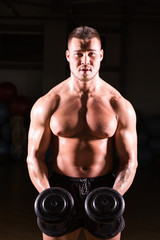 Naklejka na ściany i meble Handsome power athletic guy bodybuilder doing exercises with dumbbell. Fitness muscular body on dark background