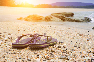 Fototapeta na wymiar Violet flip flops against the sandy beach of the brown beach on weekends.