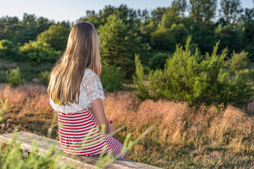 ein junges Mädchen sitz allein in der Natur auf einer Holzbank und schaut in die Landschaft