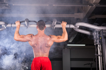 Strong man doing pull-ups on a bar in a gym.