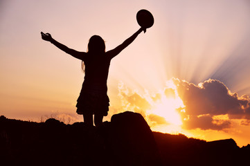 Beautiful woman with hat raise hands and enjoy in sunset. Woman on top of mountain at sunset