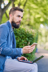 Fototapeta premium Stylish bearded male in a blue jacket using smartphone.