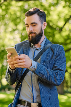 Stylish bearded male in a blue jacket using smartphone.