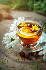 A healthy Cup of tea with lemon and rose hips and flowers on a wooden table. Selective focus.