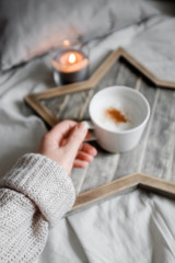 A girl in a sweater holds a cup of coffee on a designer wooden tray