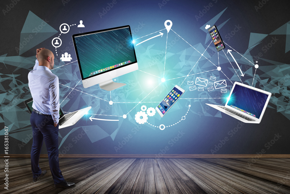 Poster businessman in front of a wall with computer and devices displayed on a futuristic interface with in