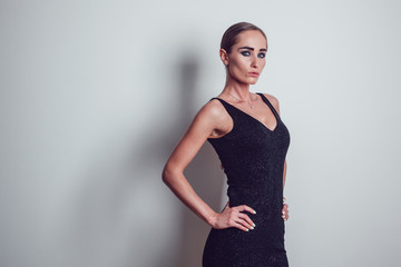 Beautiful woman in black night fashion dress posing on a gray background.