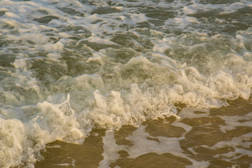 Beach sunset is a golden sunset sky with a wave rolling to shore as the sun sets over the ocean horizon
