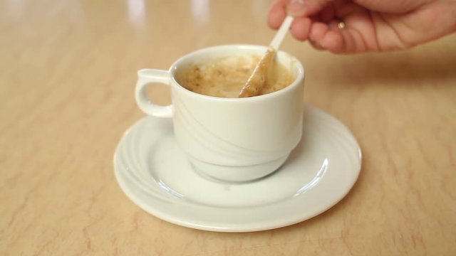 Woman's hand stirs foam on coffee with a plastic stick in a cafe, close-up.