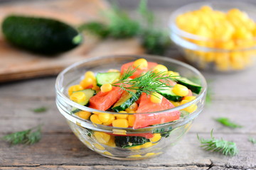 Homemade salad with fresh tomatoes, cucumbers and canned corn dressed with olive oil and lemon juice. Veggie salad in a bowl on a vintage wooden table