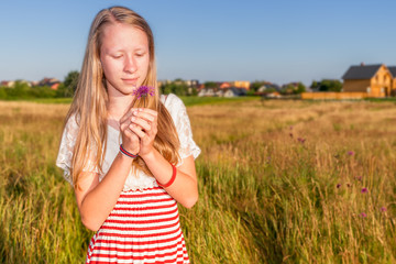 ein junges blondes Mädchen mit langen Haaren riecht an einer Blumen Blüte in der Abendsonne im Sommer