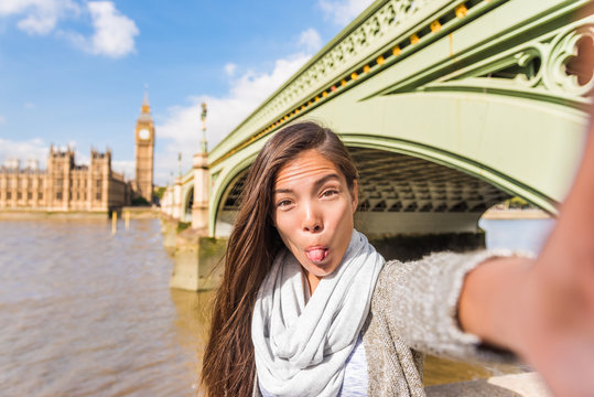 London travel selfie tourist woman making silly faces. Funny Asian girl sticking out tongue doing cheeky face for mobile phone app picture at Westminster bridge, Big Ben, UK.