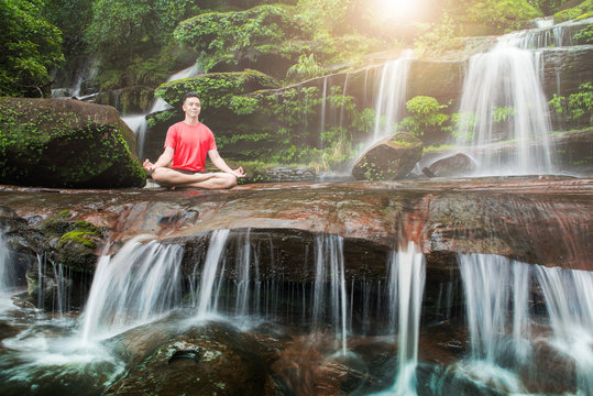 Young man meditating and relax while doing yoga on the rock between waterfalls