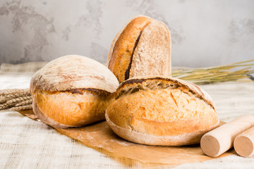 still life with a traditional round artisan wheat bread loaves, wheat and pestles on light textile background, shallow dof