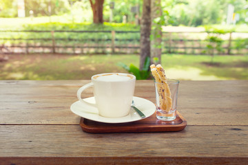 Coffee cup and pastry on wooden table with nature background.