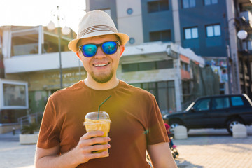 Portrait of cheerful attractive bearded hipster young man drinking iced coffee or frappe outdoors