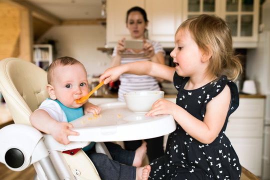 Adorable toddler girl at home feeding her baby brother.