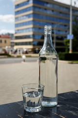 A transparent bottle and a glass of pure water on a dark wooden table of a city cafe terrace in Minsk, Belarus. Selective focus.