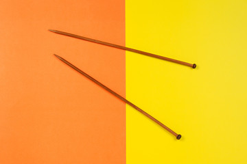 Pair of wooden knitting needles on yellow and orange background