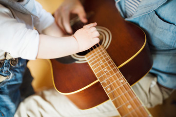 Little boy at home playing guitar with his father.