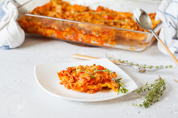 Traditional Italian lasagna baked with herbs and a piece of lasagna on a white plate.