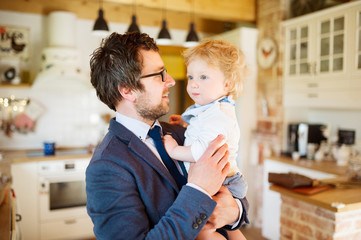 Businessman coming home, holding little son in the arms.