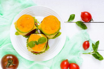 Sandwiches (burgers) with yellow and black tomatoes, juicy cutlet, avocado on a plate on a white wooden background. Top view.
