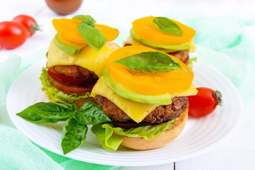 Sandwiches (burgers) with yellow and black tomatoes, juicy cutlet, avocado on a plate on a white wooden background.