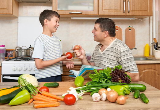 Father and son cooking and having fun with vegetables in home kitchen interior. Two people, man and child. Fruits and vegetables. Healthy food concept
