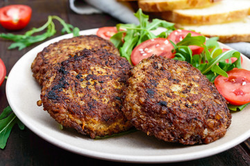 Juicy cutlets on a plate with a salad of tomatoes and arugula on a dark wooden background.