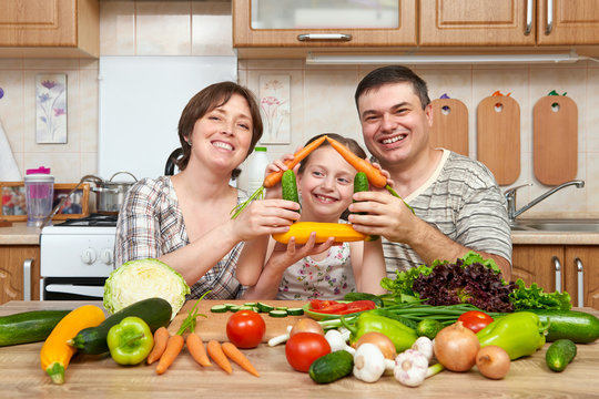 Family cooking in kitchen interior at home, fresh fruits and vegetables. Healthy food concept. Woman, man and children. Making house shape from vegetables.