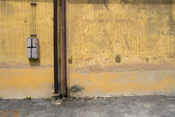 Texture of old yellow vintage wall of industrial factory with rusted iron pole and electric cable