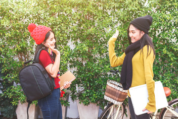 Woman student waving hello with her friend in park- friendship and togetherness concept