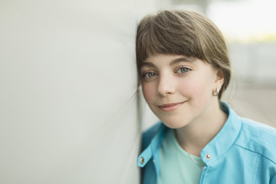 Close-up portrait of smiling girl leaning on white wall