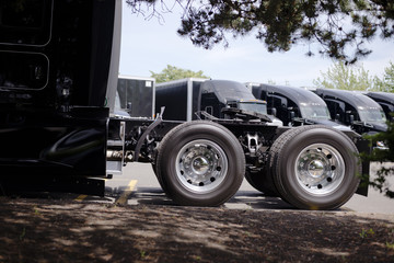 Wheels with tires of black big rig semi truck with five wheel on background of semi trucks parking lot