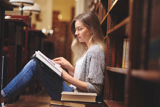 Female student reading and sitting on library floor