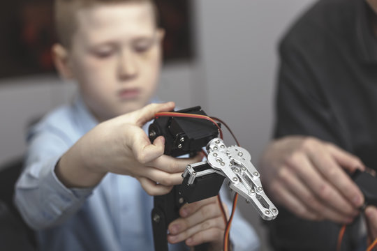 Boy operating machinery while sitting by teacher at table in classroom