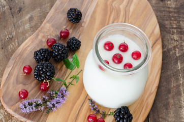 Blackberries and currants with yogurt, on wooden background.