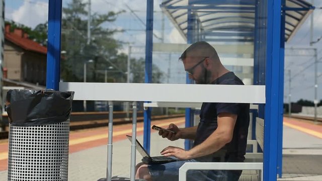 Man answers cellphone while using laptop and sitting on the bench
