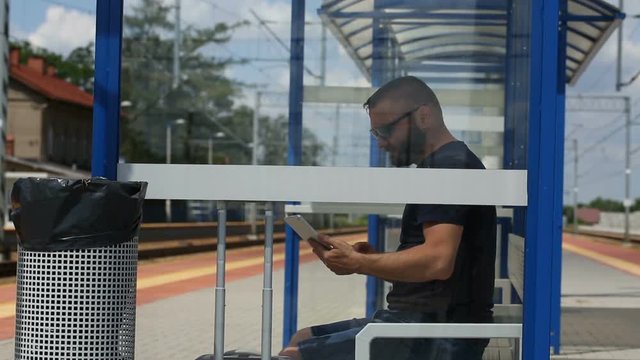Man browsing internet on tablet while sitting on the train stop and waiting for the arrival
