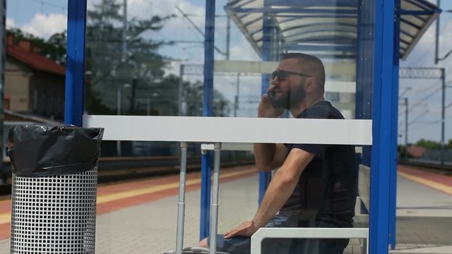 Man chatting on cellphone while sitting on the train stop and waiting for arrival
